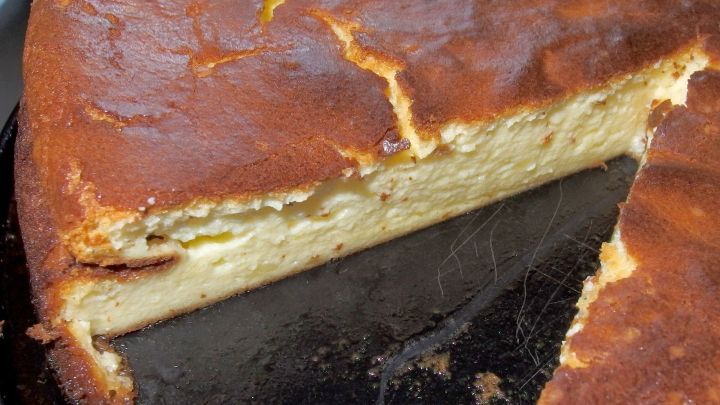 Ein goldbrauner K&auml;sekuchen ohne Boden wird gerade angeschnitten, um ein St&uuml;ck daraus zu servieren.
