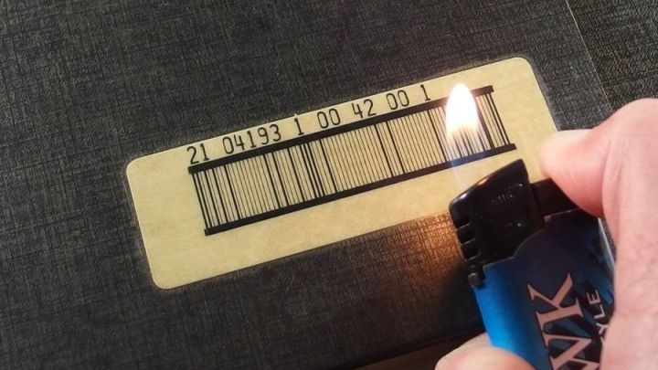 Ein Feuerzeug entfernt einen Aufkleber von einem Buch, w&auml;hrend eine Hand das Feuerzeug h&auml;lt, um die Klebeeigenschaften zu l&ouml;sen.