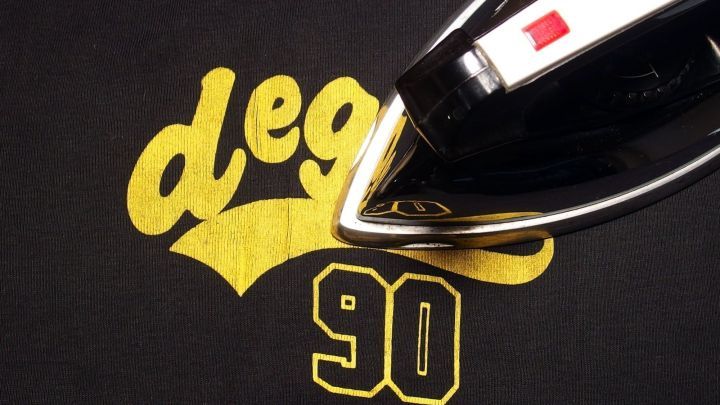 Ein schwarzes T-Shirt mit gelbem Aufdruck wird mit einem B&uuml;geleisen bearbeitet, um den Druck zu gl&auml;tten.