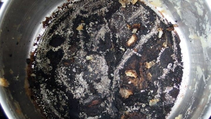 Ein verschmutzter Topf mit eingebrannten R&auml;ndern liegt auf einer Arbeitsfl&auml;che und zeigt Reste von Lebensmittelverkrustungen.