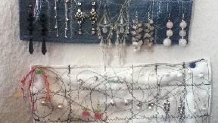 Ein selbstgen&auml;hter Ohrringhalter h&auml;lt diverse Ohrringe auf strukturiertem Stoff an einer Wand zur Schau.