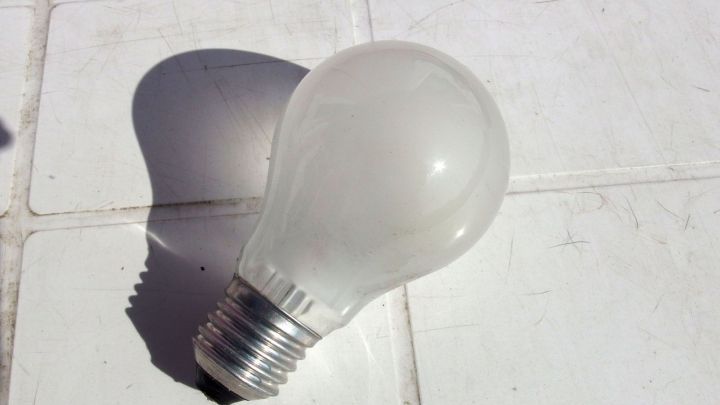 Eine Gl&uuml;hbirne liegt auf einer wei&szlig;en Oberfl&auml;che, bereit zum Austauschen, w&auml;hrend ihr Schatten darunter sichtbar ist.