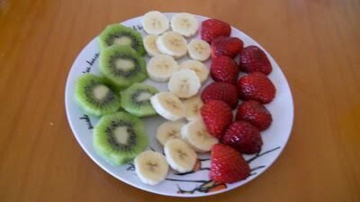 Kiwi-, Bananen- und Erdbeerscheiben sind dekorativ auf einem Teller arrangiert, auf einem Holztisch liegend.