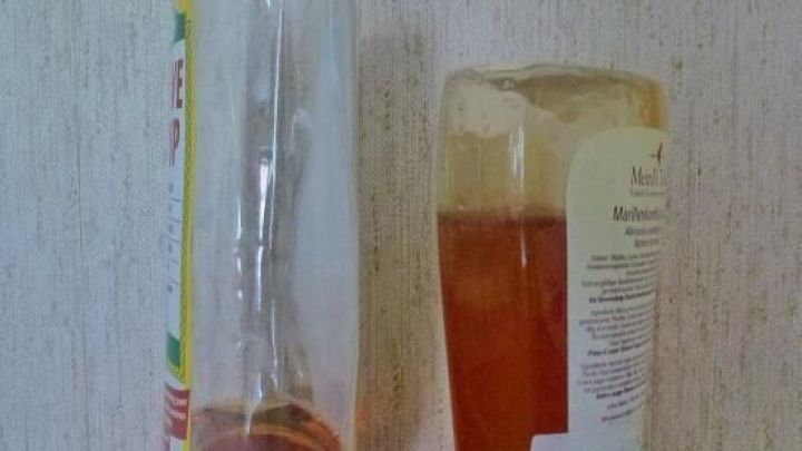 Zwei Honigspender stehen verkehrt herum auf einer dunklen Oberfl&auml;che. Der eine ist fast leer und der andere ist halbvoll.