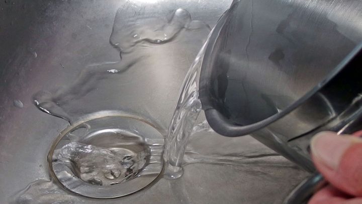 Wasser wird aus einem Beh&auml;lter in ein Sp&uuml;lbecken gegossen, das einen verstopften Abfluss hat, um die Verstopfung zu l&ouml;sen.