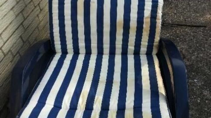 Ein Sonnenliegenauflage mit blauen und wei&szlig;en Streifen liegt schmutzig auf einer Liege im Au&szlig;enbereich.