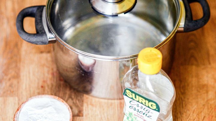 Ein gl&auml;nzender Topf steht auf einem Holzuntergrund, daneben Essig und eine Schale mit Pulver f&uuml;r die Reinigung.