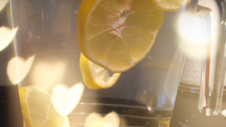 Zitronen schwimmen in einem Glas Wasser, umrahmt von herzf&ouml;rmigen Lichtern auf einem K&uuml;chentisch.