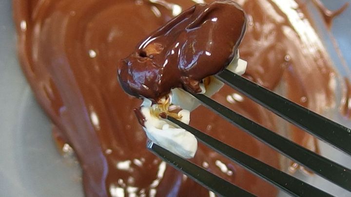 Ein Popcornst&uuml;ck wird mit einer Gabel in geschmolzene Schokolade getaucht, w&auml;hrend die Schokolade in einer Sch&uuml;ssel ruht.