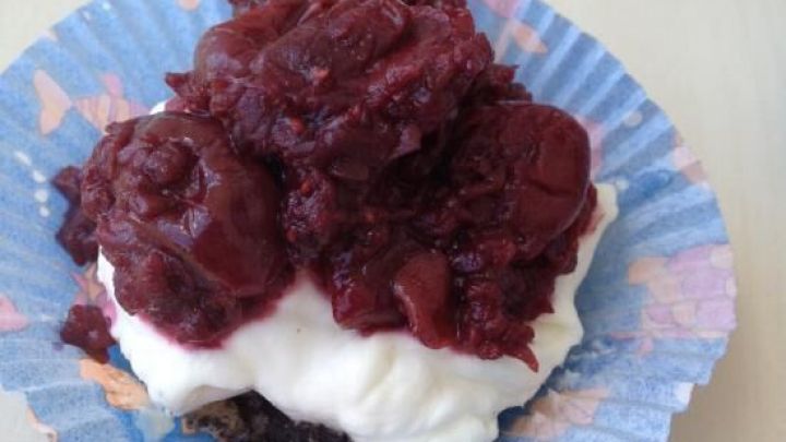 Ein Kirsch-Quark-Muffin steht auf einem blauen Papierf&ouml;rmchen, bedeckt mit fruchtigem Kirschkompott und Quark.