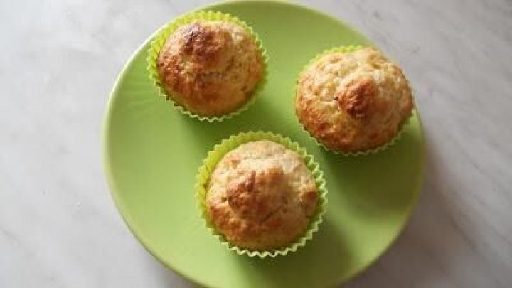 Drei goldbraune Brioche-Muffins ruhen in gr&uuml;nen F&ouml;rmchen auf einem hellgr&uuml;nen Teller, platziert auf einer wei&szlig;en Unterlage.