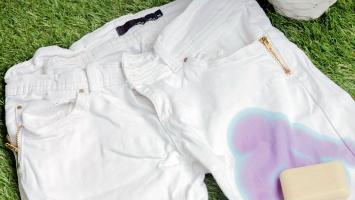 Weiße Jeans mit Pflanzenfleck liegen auf grünem Gras, daneben steht ein Stück Seife für die Fleckenentfernung.