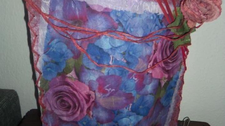 Eine selbst gestaltete Lampe aus buntem Papier mit Blumenmuster steht dekorativ auf einem Holztisch an einer Wand.