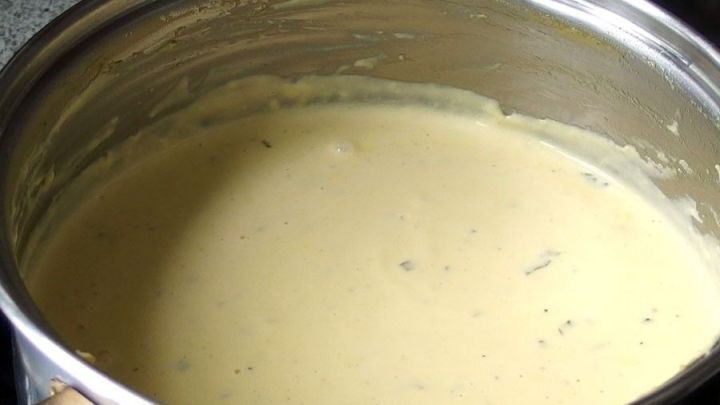 Eine cremige Sauce Hollandaise k&ouml;chelt in einem Topf auf dem Herd, umgeben von einer k&uuml;chen&auml;hnlichen Umgebung.