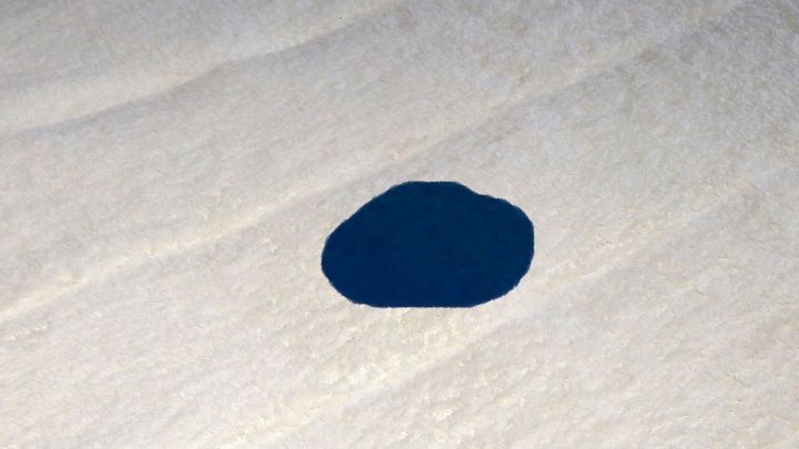 Ein blauer Tintenfleck liegt auf einem hellen, glatten Untergrund und deutet auf m&ouml;gliche Verschmutzung hin.
