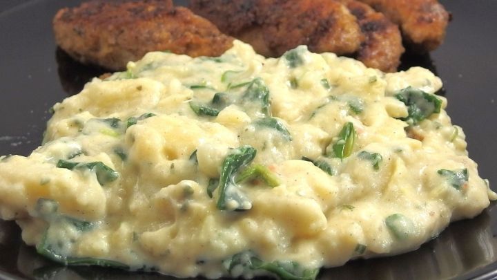 Ein cremiger Kartoffelsalat ohne Mayonnaise liegt auf einem Teller neben knusprigen Schnitzeln in einer gem&uuml;tlichen K&uuml;che.