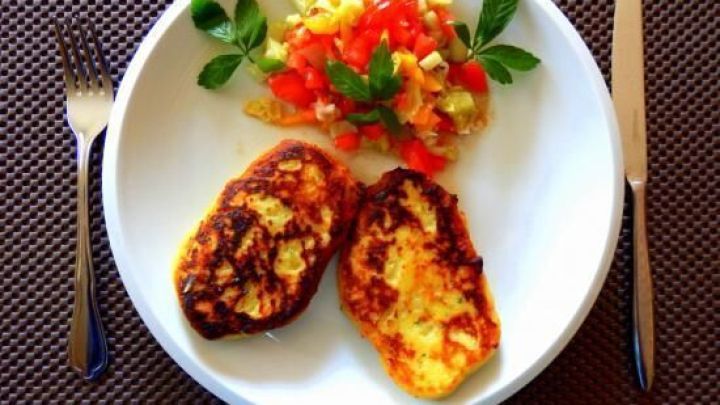 Kartoffel-Buletten liegen auf einem Teller neben einem frischen Salat mit Tomaten und Kr&auml;utern auf einem Tischset.