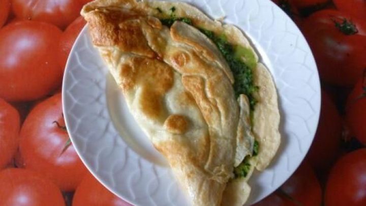 Ein halb gefalteter Eierpfannkuchen liegt auf einem Teller und ist mit Spinat gef&uuml;llt, pr&auml;sentiert auf einem Tomatenuntersetzer.