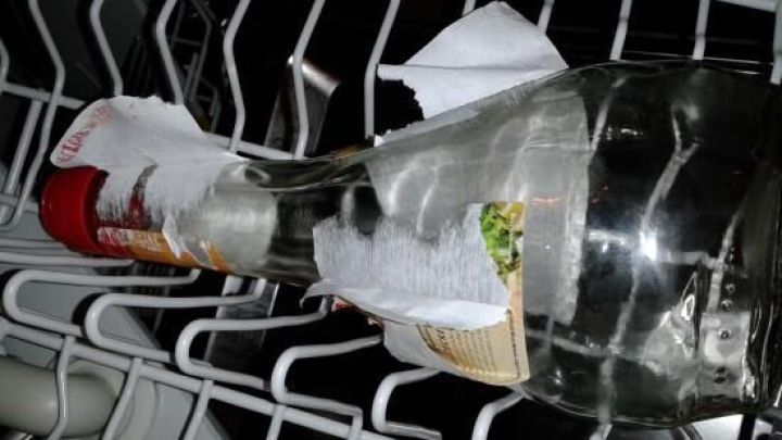 Eine Marmeladenglasflasche liegt in einem Geschirrsp&uuml;ler und hat ein angefeuchtetes K&uuml;chenpapier um den Etikett-Bereich gewickelt.