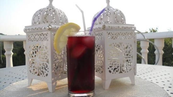 Ein Glas Tinto de Verano mit Zitronenscheibe steht auf einem Tisch zwischen dekorativen wei&szlig;en Laternen im Freien.