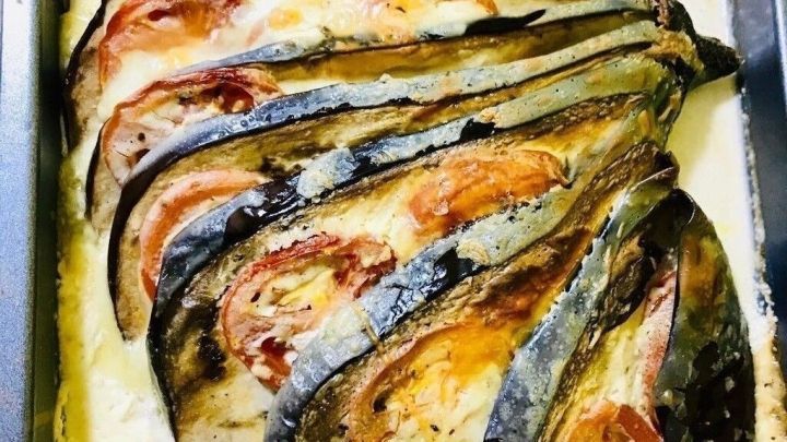 Ein leckerer Auberginenauflauf liegt frisch gebacken in einer Auflaufform, mit geschichteten Auberginenscheiben und Tomaten.
