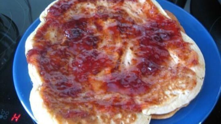 Fluffige Doppeldecker Pfannkuchen liegen auf einem blauen Teller, bedeckt mit einer dicken, fruchtigen Sauce im Hintergrund.