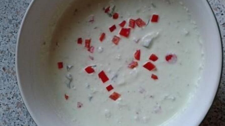 Eine Sch&uuml;ssel mit cremigem Dip, bestreut mit roten Paprikast&uuml;cken, steht auf einer gesprenkelten K&uuml;chenarbeitsplatte.