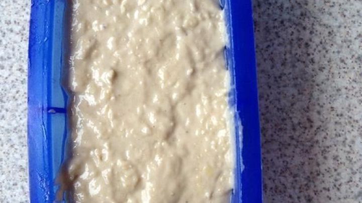 Vegan Bananenbrot-Mischung ist in einer blauen Form platziert, bereit zum Backen auf einer hellen K&uuml;chenoberfl&auml;che.