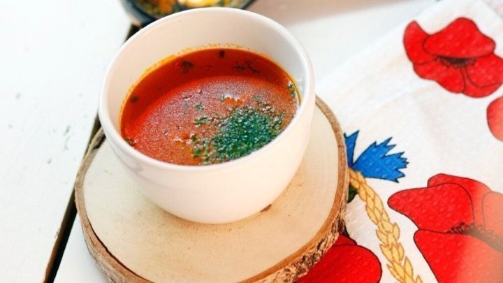 Eine Sch&uuml;ssel kalte Rote Beete Suppe steht auf einem Holzuntersetzer, umgeben von einer bunten Serviette und einem L&ouml;ffel.