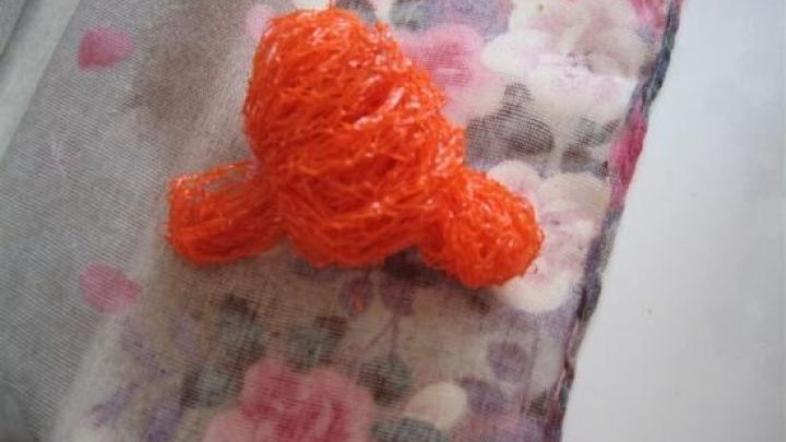 Ein orangefarbenes Zwiebelnetz liegt als improvisiertes Abwaschtuch auf einem pastellfarbenen, floralen Stoff.