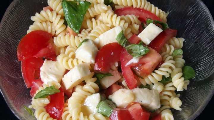 Eine Sch&uuml;ssel Pasta mit Tomaten und Mozzarella mischt frische Zutaten und zeigt eine bunte, sommerliche Mahlzeit.