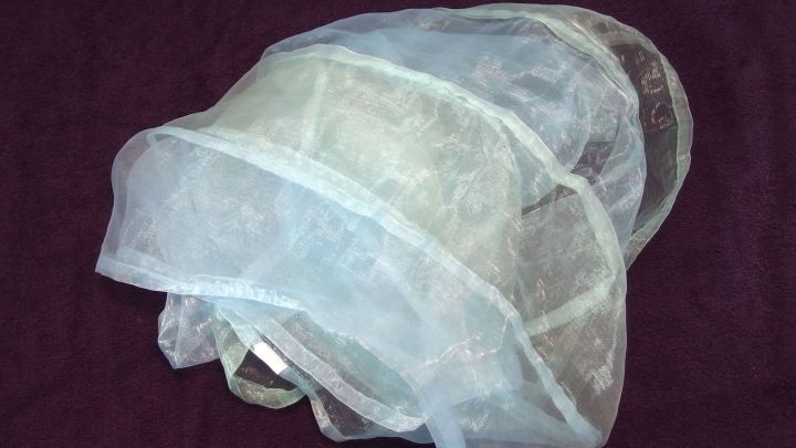 Ein W&auml;schenetz aus feinem Stoff liegt gefaltet auf einem dunklen Untergrund, bereit zum N&auml;hen und Verschlie&szlig;en.