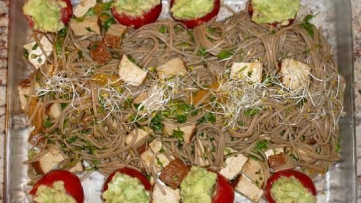 Ein bunter vegetarischer Salat aus Buchweizennudeln, Tomaten und Tofu auf einem Tablett, angereichert mit frischen Sprossen.