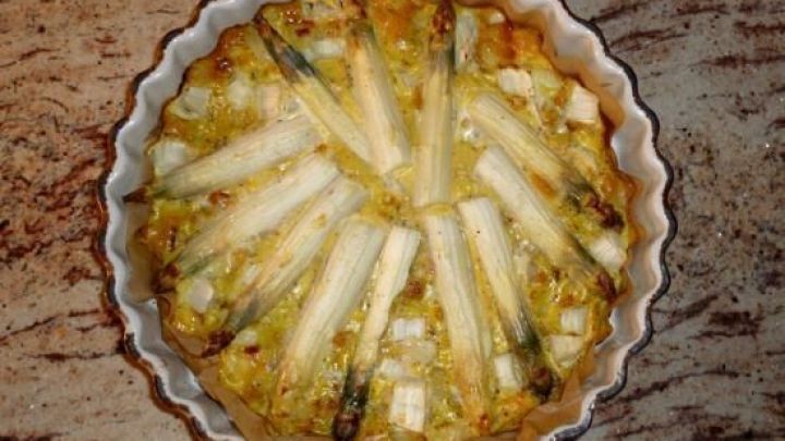 Eine goldbraune Kartoffel-Spargel-Tortilla aus dem Backofen liegt in einer runden Form auf einem hellen Tisch.