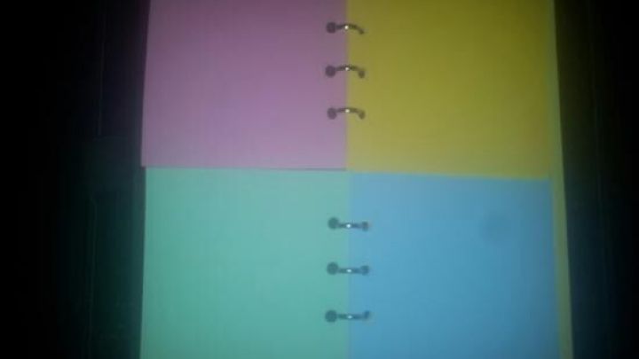 Bunte Filofax Notizbl&auml;tter liegen gestapelt, mit Ringen gebunden, auf einem dunklen Tisch im Hintergrund.