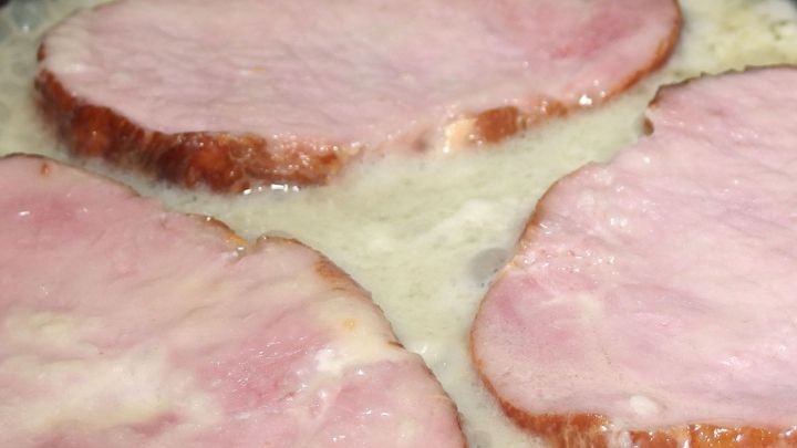 Dicke Kassler Koteletts brutzeln in einer Pfanne, umgeben von schmelzendem Fett und einer goldbraunen Kruste.