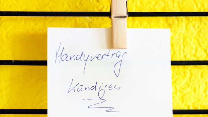 Ein Notizzettel mit "Handyvertrag" und "k&uuml;ndigen" ist an einer Schnur vor einer leuchtend gelben Wand befestigt.