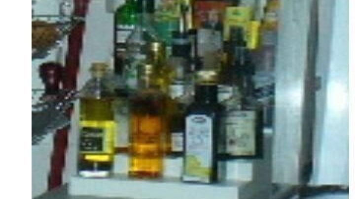 Flaschen mit So&szlig;en und &Ouml;len stehen geordnet auf einem Regal in der K&uuml;che neben dem Herd.