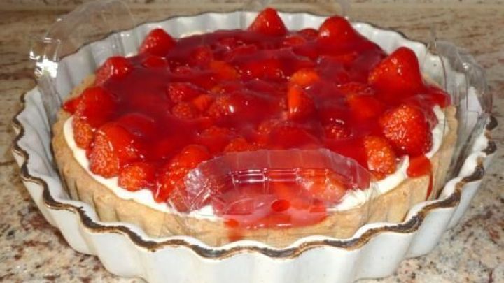 Erdbeerkuchen steht in einer geriffelten Keramikform und ist mit einer durchsichtigen Plastikkuppel vor Besch&auml;digung gesch&uuml;tzt.