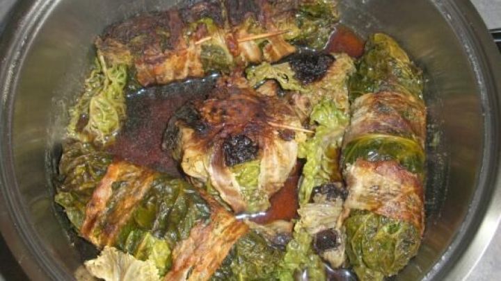 Kohlrouladen, umwickelt mit Fr&uuml;hst&uuml;cksspeck, garen in einem Topf und zeigen eine goldbraune, knusprige Oberfl&auml;che.