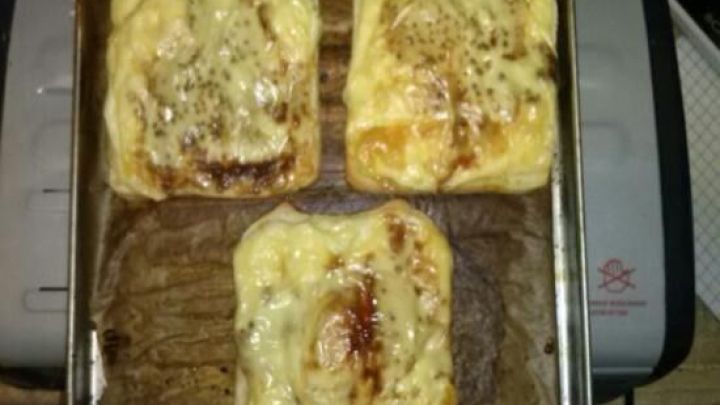 Drei K&auml;se-Eier-Snacks backen auf einem Blech im Ofen, mit leicht brauner Kruste und Gew&uuml;rzen bestreut.