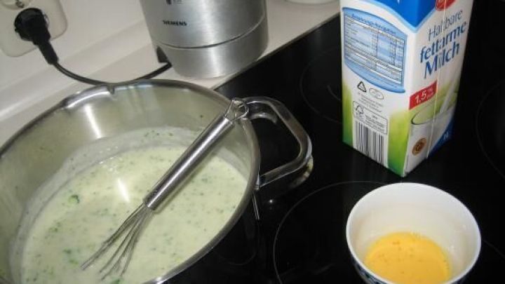 Ein Schneebesen r&uuml;hrt in einer Sch&uuml;ssel mit Eiwei&szlig; und Kr&auml;utern, daneben stehen H-Milch und eine Tasse mit rohem Ei.