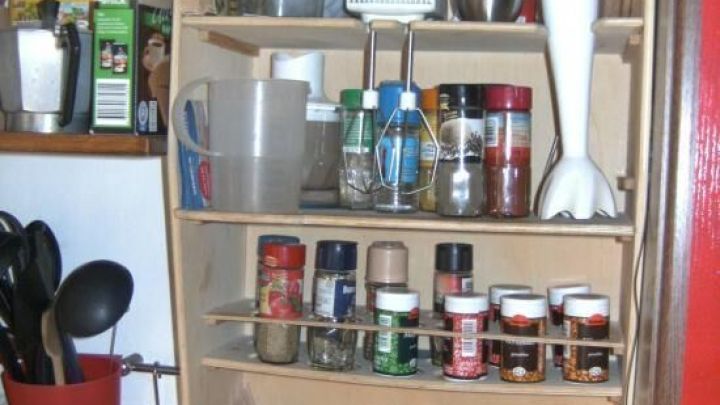 Ein Holzregal mit R&uuml;hrger&auml;ten und Gew&uuml;rzen ist an der K&uuml;chenwand montiert, um K&uuml;che und Utensilien zu organisieren.