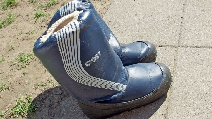 Ein Paar blaue Stiefel mit der Aufschrift "SPORT" steht auf einem sonnigen Pflasterweg. Links ist etwas Gras zu sehen.
