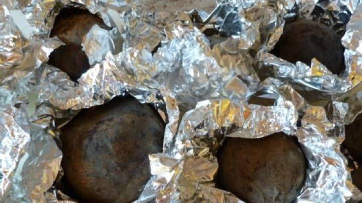 Rote-Bete-Knollen ruhen in teilweise ge&ouml;ffneten Alufolienb&uuml;ndeln auf einer Tischplatte, bereit zum Garen.