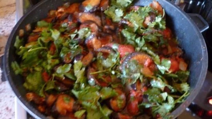 Eine Pfanne mit frischen, gehackten Auberginen, Tomaten und Koriander, die auf dem Herd k&ouml;chelt.