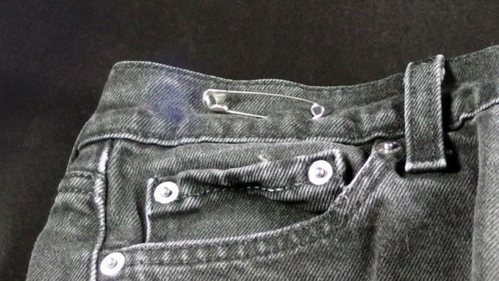 Eine schwarze Hose mit einem defekten Knopf, die auf einem dunklen Hintergrund liegt, zeigt die Dringlichkeit einer schnellen Hilfe.