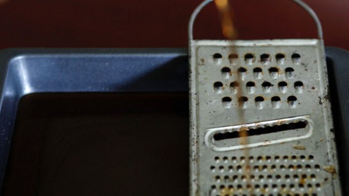 Eine rostige Metallreibe liegt in einer Sch&uuml;ssel mit Cola, die zur Rostentfernung verwendet wird.