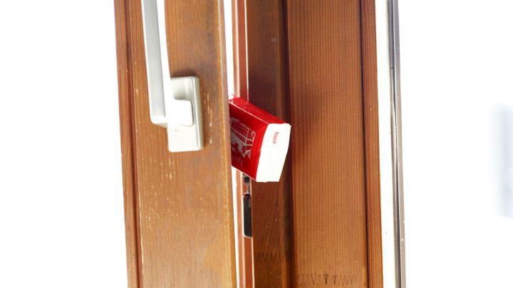 Ein Kippfenster steht leicht ge&ouml;ffnet, w&auml;hrend ein rotes Objekt zwischen den Rahmen klemmt, um das Schlie&szlig;en zu verhindern.