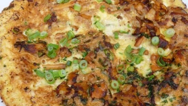 Ein goldbraunes Pfifferling-Omelette liegt auf einem Teller, garniert mit frischen Fr&uuml;hlingszwiebeln, appetitlich angerichtet.